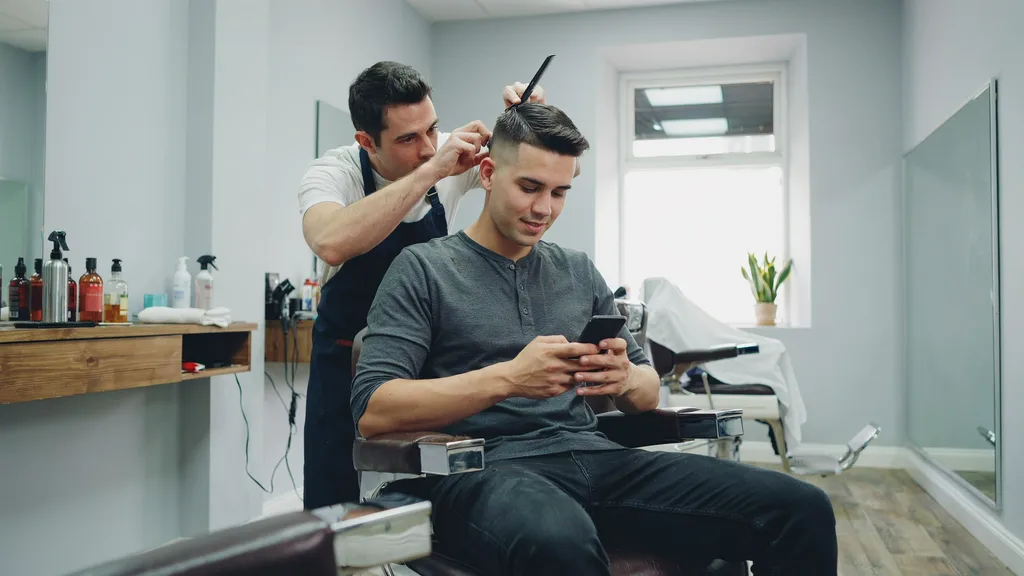Young man with a fade checking his phone in a modern barbershop