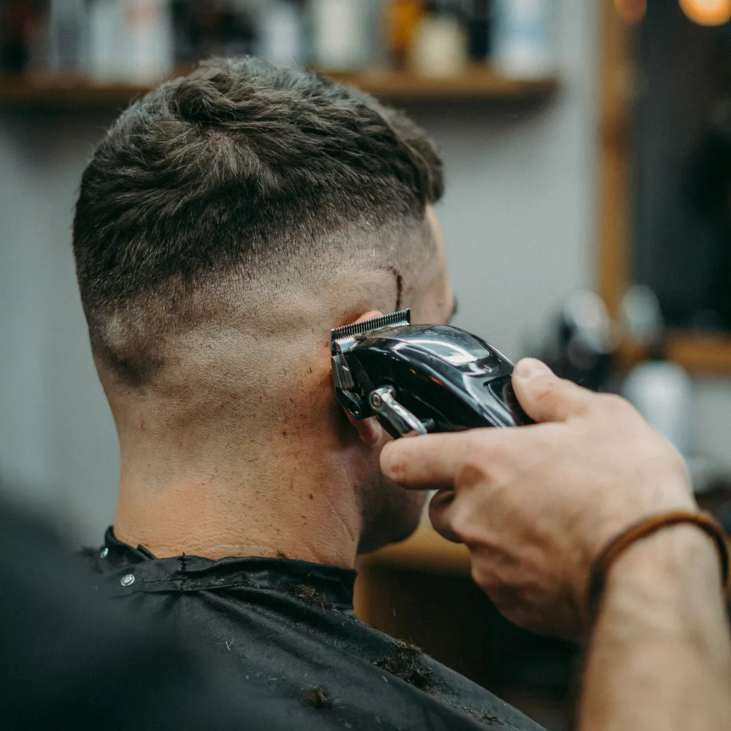 Barber's clippers blending hair at temple level for a mid fade