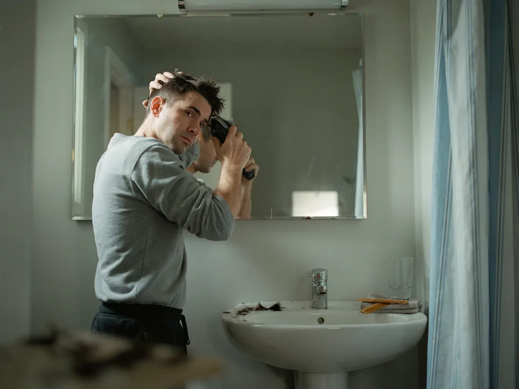 Man cutting his own mid fade haircut with clippers in a home mirror