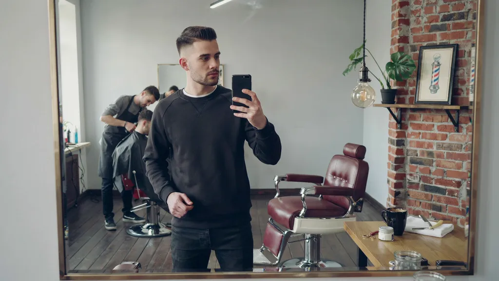 Young man with a mid fade taking a mirror selfie in a barbershop