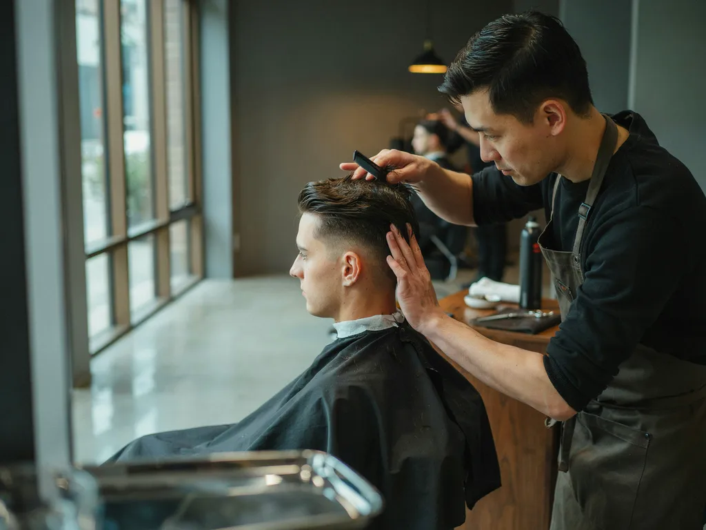 Barber combing and styling the top hair of a mid fade haircut