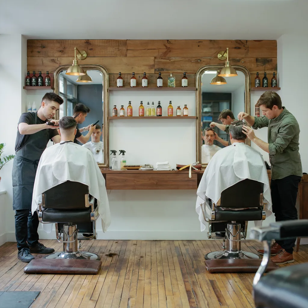 Two barber chairs in a modern barbershop with different haircuts being styled