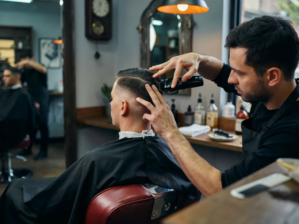 Barber blending hair at the temple with clippers side profile view